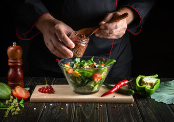 Professional chef prepares a salad of fresh vegetables. Menu concept for hotel on black background. Adding aromatic spices to a salad