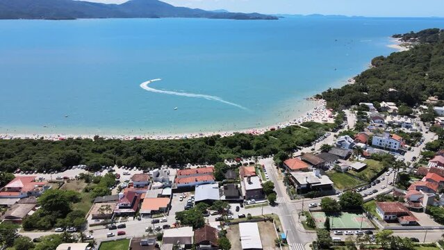 Drone aerial scene of paradise beach with boat doing stunts in ocean and tropical urban beach mesh Florianópolis