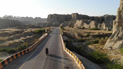 Motorcyclist Riding Into Distance On Makran Coastal Highway Road Beside Dramatic Rock Formations In Hingol National Park. Aerial Shot