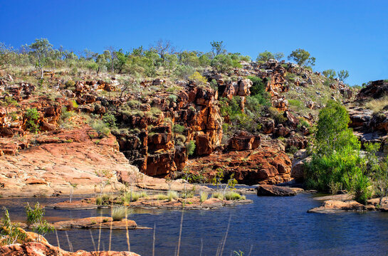 Nature photographer on a hiking trip at the Australian outback at bell gorge billabong on rocky environment between Eucalyptus tree, boulders and hills at the morning light 