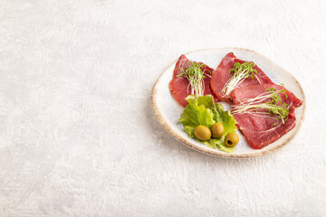 Slices of smoked salted meat with cilantro microgreen on gray. Side view, copy space.