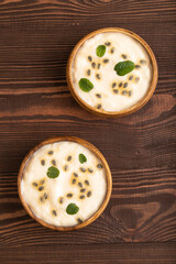 Yoghurt with granadilla and mint in wooden bowl on brown wooden, top view.