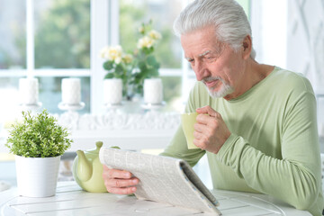 Emotional senior man reading newspaper posing at home
