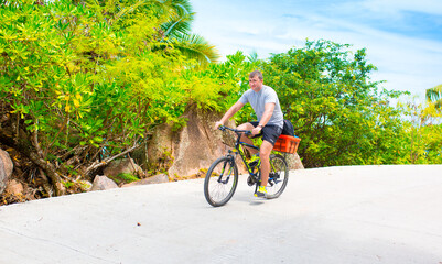 Happy young guy riding a bike on the road by the sea in the Seychelles. Concept of vacation and...