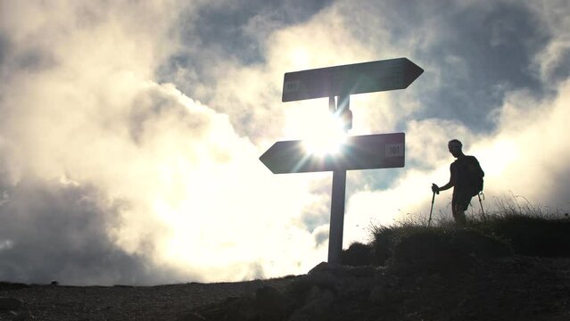 Trekker at mountain crossroad with signs walking down with backpack, boots and trekking poles. Clouds moving on the background. Abruzzo Italy.