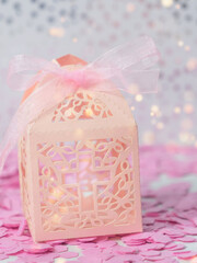 Paper gift box on a pink background and bokeh. Cross Cut Paper Packing Souvenir Box for Candy, Dragee for Holiday, Girl's Baptism, Birthday, Easter, First Communion, Wedding Table Decoration.