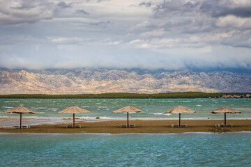 Nin, Croatia - Empty Queen's Beach by the little mediterranean town of Nin at the end of summer with reed sunshades, Velebit Mountains at background and turquoise Adriatic sea water on an autumn day