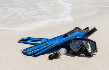 Mask and fins for scuba diving and snorkeling lie on the sandy shore against the backdrop of the sea and ocean.