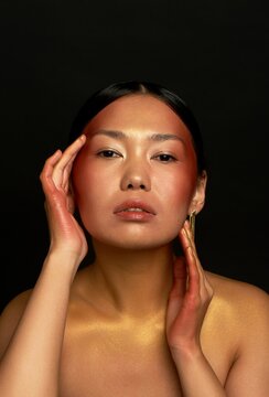 An Asian girl on a black background in the studio. Gold. Thin collarbones. Long gold earrings. The realm of beauty and perfume