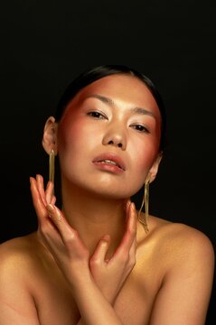 An Asian girl on a black background in the studio. Gold. Thin collarbones. Long gold earrings. The realm of beauty and perfume