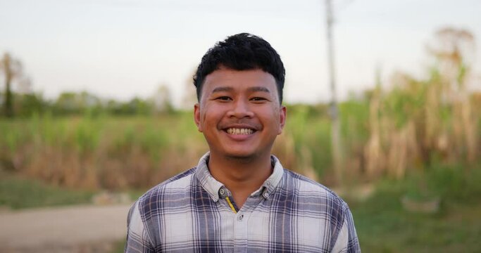 Portrait of an Asian young happy farmer man looking at camera and smiling with a farmland background. Agriculture farming concept. Slow motion.