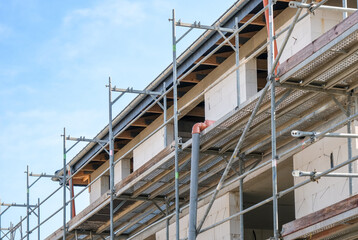 Konzept Investition Wohnungsbau: Detail des Rohbaus eines großen Hauses mit Gerüst, Abfluss und anderen Materialien, seitliche Ansicht mit viel blauem Himmel und Textfreiraum