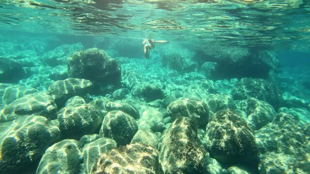 Young woman in bikini swimming underwater with rocky sea floor near Ponza island in Italy
