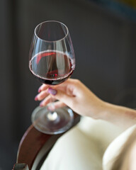 Glass of red wine in woman's hand. Rest in solitude. Woman is drinking wine. Drink enjoyment. Italian wines. Alcoholic drink. Dark background. View from above. Soft focus. Copy space.