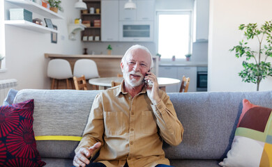 Senior man chatting on a mobile phone while relaxing on a sofa in his living room. Happy senior man talking on phone in the living room.