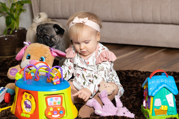 A happy one-and-a-half-year-old girl plays with toys sitting on the floor.