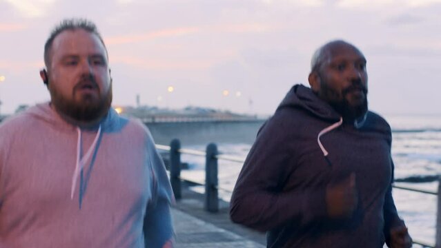 Man, runner friends and overweight at beach for training, exercise or workout for health at sunset. Men, running partnership and wellness team by ocean, together and support for obesity in Seattle