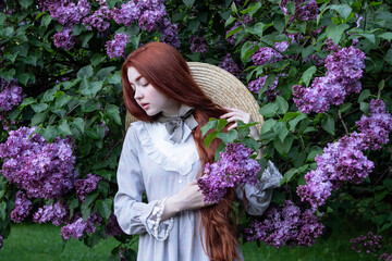 young girl with long red hair with lilac flowers  in the garden in spring