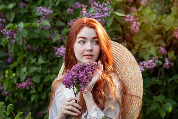 young girl with long red hair with lilac flowers  in the garden in spring