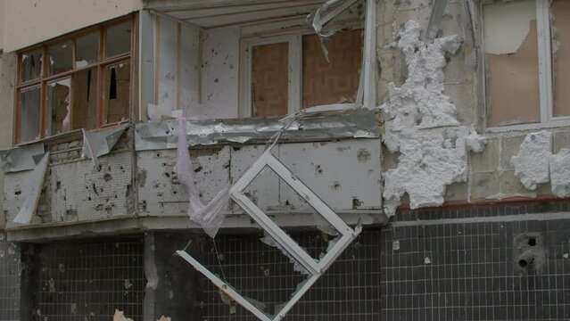 Broken window hanging of destroyed balcony. War in Ukraine. Shattered glass caused by a shock wave after russian missile hit on block of flats. Russian shooting civilian houses in Kharkiv 25.05.2022