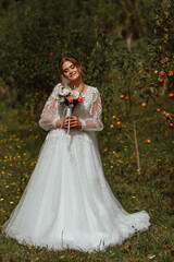 a young beautiful bride poses with a wedding bouquet against the background of nature; the girl is dressed in a white wedding dress; a moment on the wedding day; happy girl expresses her emotions