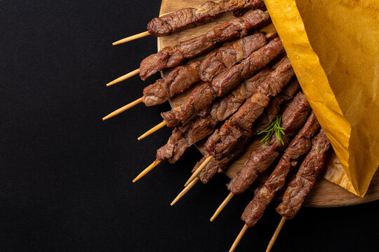 Lamb skewers or kebabs cooked on a brazier, with rosemary and spices.  Arrosticini, italian meat dish. Black background, wooden board, copy space.