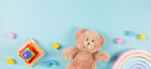 Baby kids educational toys frame background. Teddy bear, wooden stacking pyramide tower, toy rainbow and colorful blocks on light blue background. Top view, flat lay