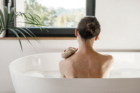 Woman looking at window while she taking a bath, washing body with sponge