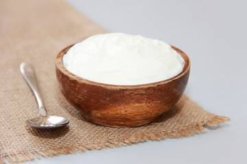 Fototapeta na wymiar Natural white fermented milk yogurt in a wooden plate next to a metal spoon