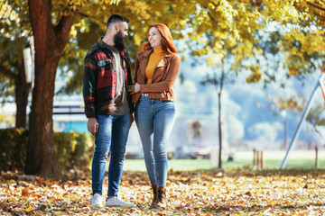 Young happy couple looking at each other while holding hands and walking in the park.