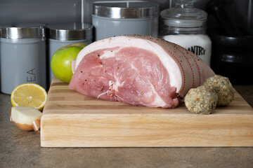 uncooked Leg of Pork joint on a beech block cutting board with onion, lemon  cooking apple and sage...