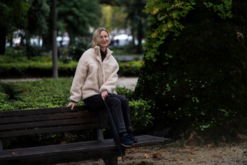 Fototapeta premium A woman sits on a bench in an autumn park.