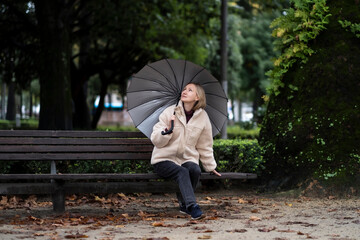 A woman with an umbrella sits on a bench in an autumn park.