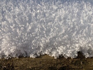 white crystal snow lies on a brown wooden beam