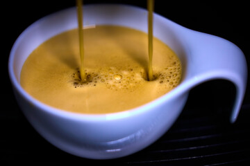 Frischer Kaffee wird zubereitet, cremiger Kaffee rinnt in eine weisse Tasse.