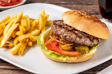 Delicious grilled homemade hamburger with beef, tomatoes, cheese, and lettuce on rustic wooden background