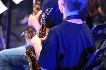 Portrait of a teenage boy holding a saxophone sitting in an orchestra close-up rear view