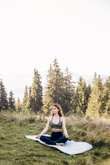 Flexible girl doing yoga in the mountains among the fir trees on a sunny day.