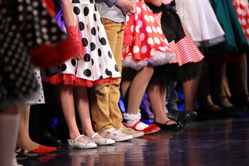 A group of children of small artists a boy and girls in bright colorful dresses stand on the stage in a row