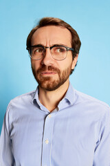 Half-length portrait of mature bearded man in eyewear expressing vivid emotions on his face isolated over blue background. Business, mental health, emotions concept