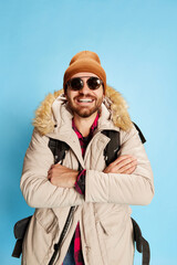 Fashionable mature man in winter coat and hat with happy facial expression looking at camera isolated on blue background. Holidays, travel, adventure, ad