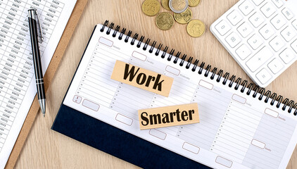 WORK SMARTER word written on wooden block on planner with coins, clipboard and a calculator