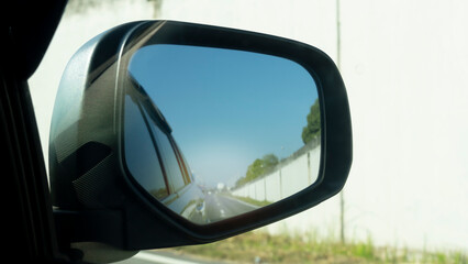 Wing mirror view of car on the road. With reflections of Cement panel over the road bridge. Environment in the day bright.