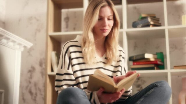 Dreamy soft shot of young charming blond woman reading book story in cozy living room Attractive female enjoying leisure time weekend with literature novel at home alone