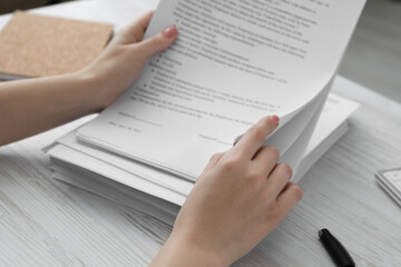 Woman reading documents at white wooden table in office, closeup