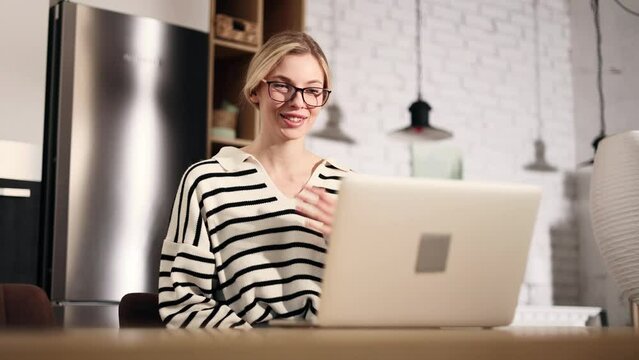 Beautiful young blond woman with glasses has video call conference meeting interview by laptop computer at home apartment Smiling lady talking on working or personal conversation indoors