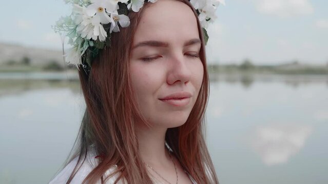 Portrait of a beautiful young woman in a wreath of flowers against the backdrop of wildlife and lake. The face of a happy positive person