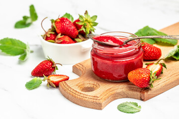 Strawberry jam in the glass jar with a spoon at white table. top view
