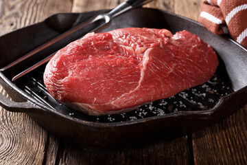 Raw piece of meat for grilling with vegetables in a cast iron pan, close-up, eating out, studio photo