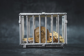Cryptocurrency Bitcoin in a cage among other coins close-up on dark background.